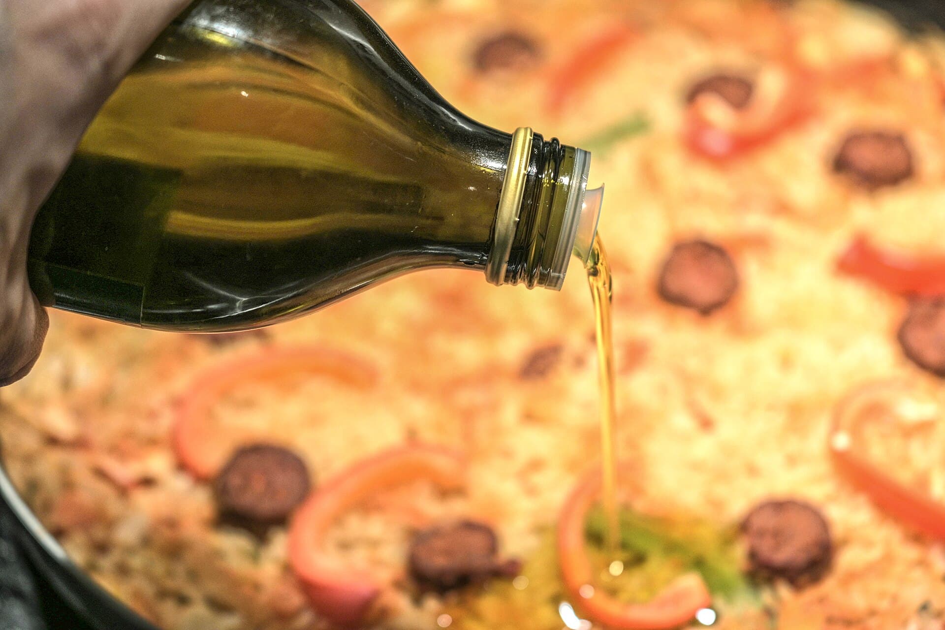 Olivolja hälls över pizza, extra virgin som både bakfett och avslut i köket